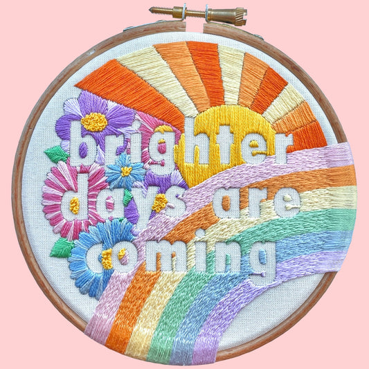 An embroidery kit with the phrase 'brighter days are coming' surrounded by colorful floral designs, displayed in an embroidery hoop.