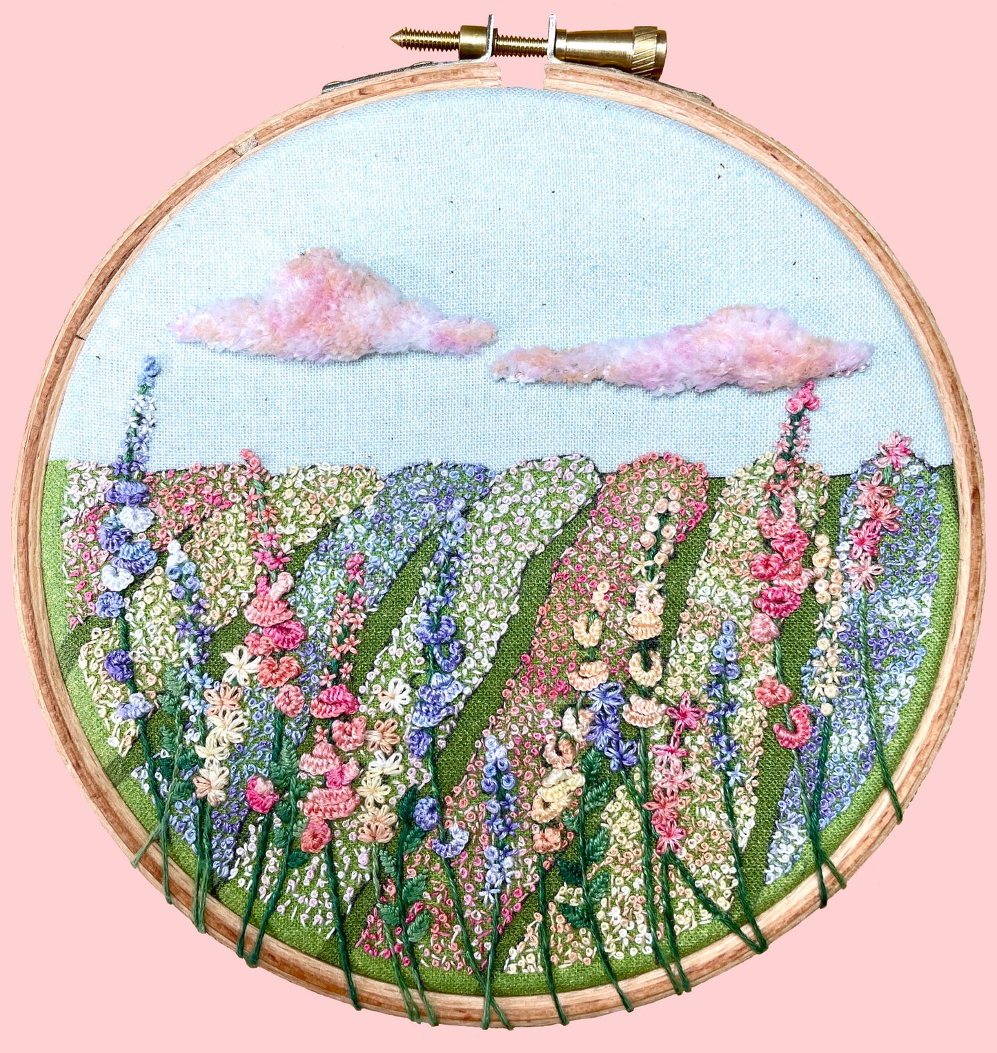 Embroidery kit depicting a field of flowers with blue, pink, and purple hues, stitched in a hoop.