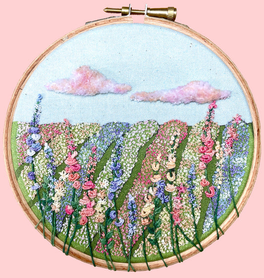 Embroidery kit depicting a field of flowers with blue, pink, and purple hues, stitched in a hoop.