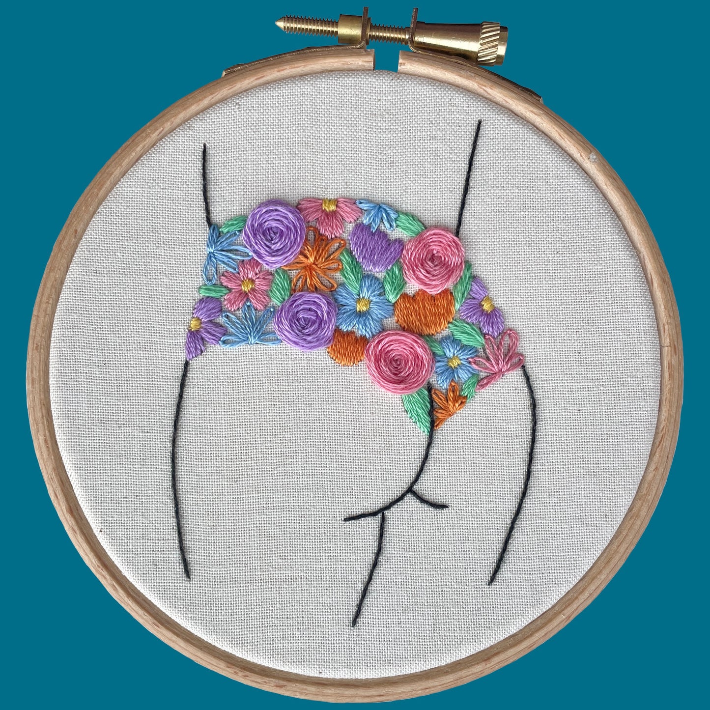 Embroidery hoop with a colourful floral knicker design on natural calico fabric against a teal background.