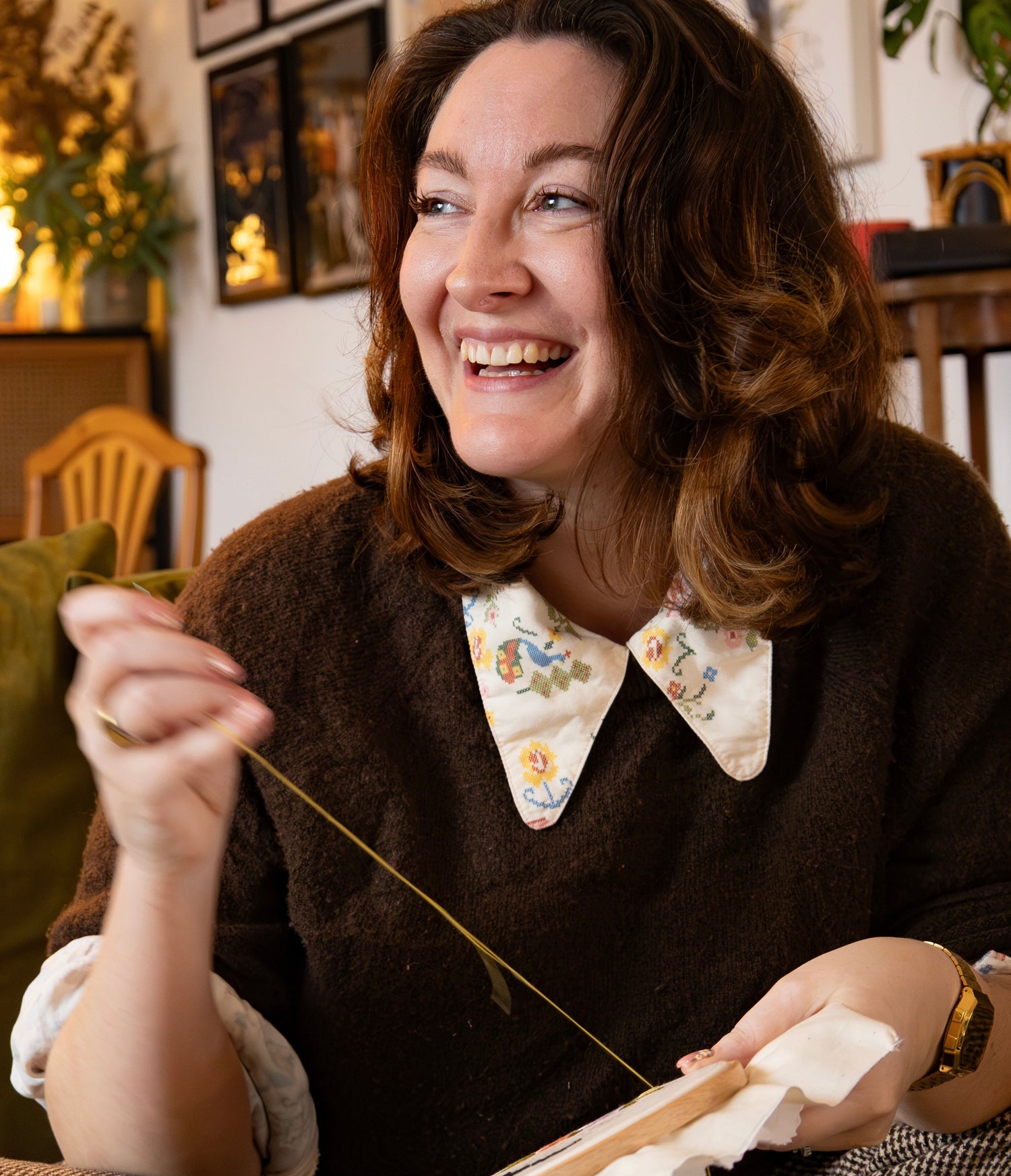 Woman sitting in a cozy room, holding knitting needles and smiling.