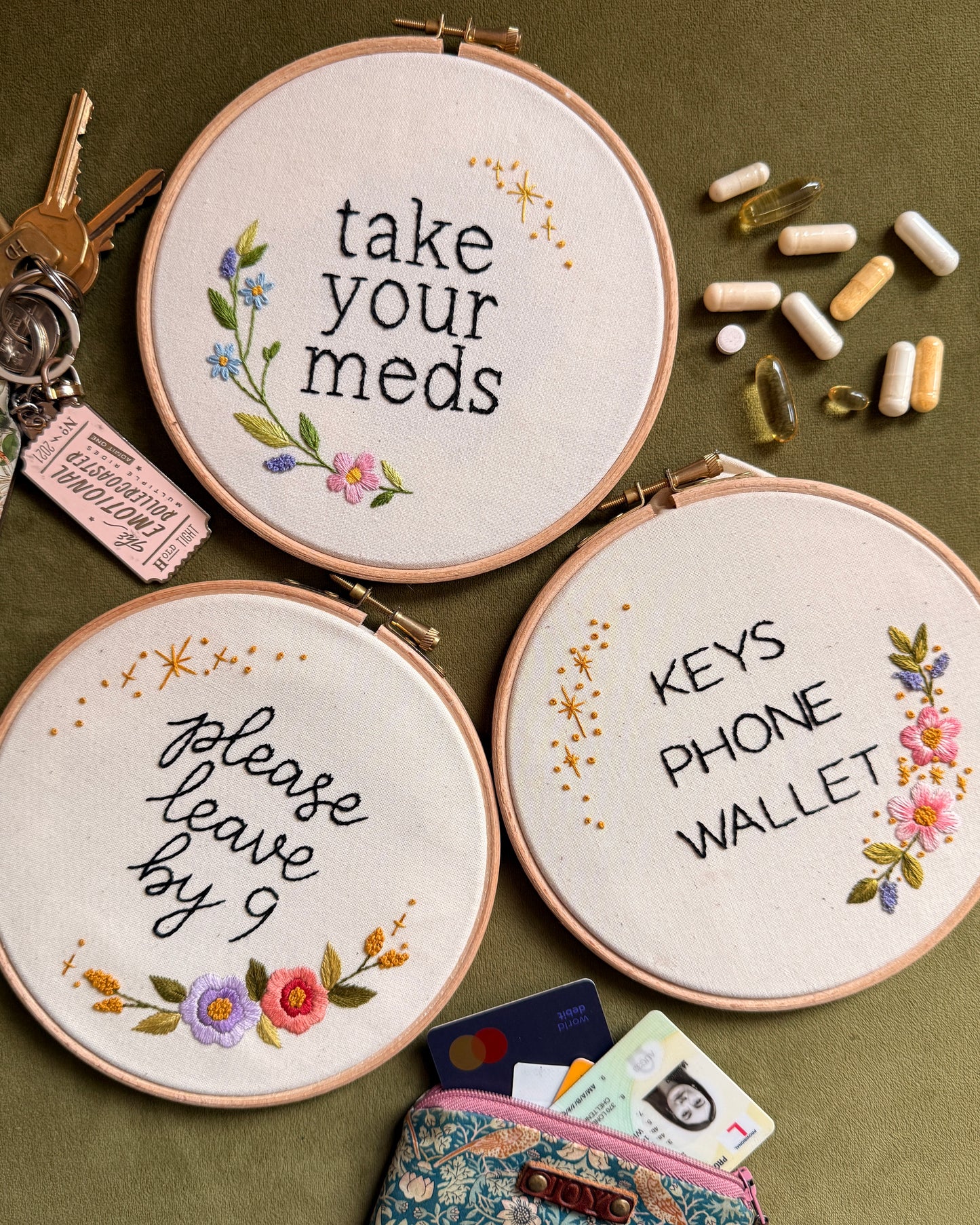 Three embroidered hoops with humorous text and floral designs on a green background.