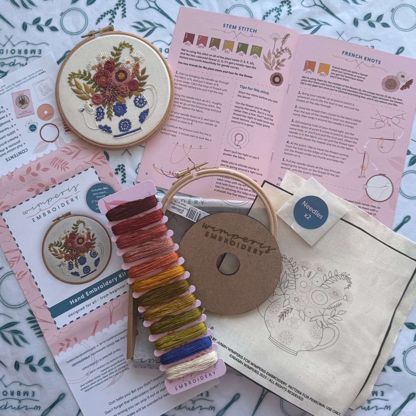 Embroidery kit with thread, hoop, and pattern sheets on a floral fabric background