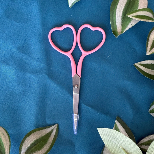 Pink scissors with heart-shaped handles on a blue fabric background with leaf patterns