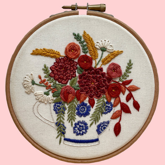 A completed floral embroidery hoop featuring a detailed and colorful floral design on white fabric, set within a wooden hoop.