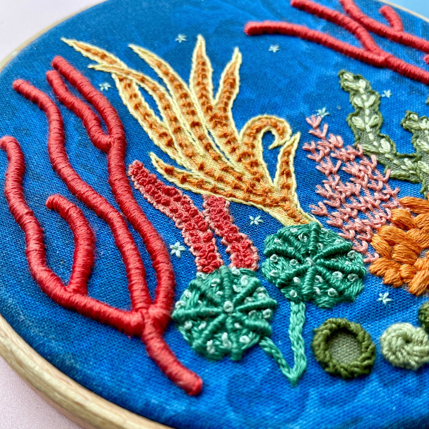 Embroidery hoop with colourful underwater scene with coral on blue fabric.