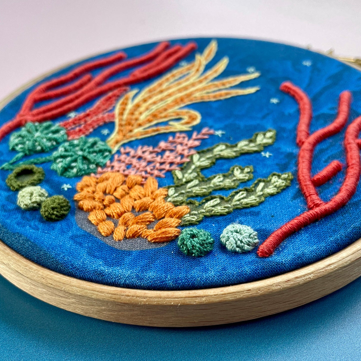 Embroidery hoop with colourful coral reef design on a blue fabric background