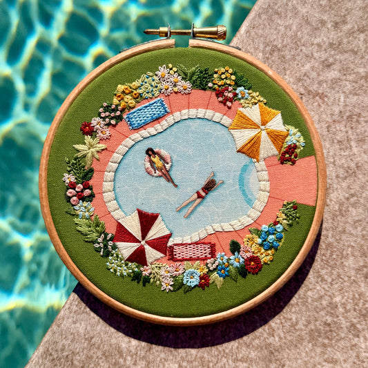 Embroidery hoop with a poolside scene by a pool