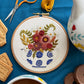Embroidery hoop with floral design on a blue surface with sewing tools and tea.