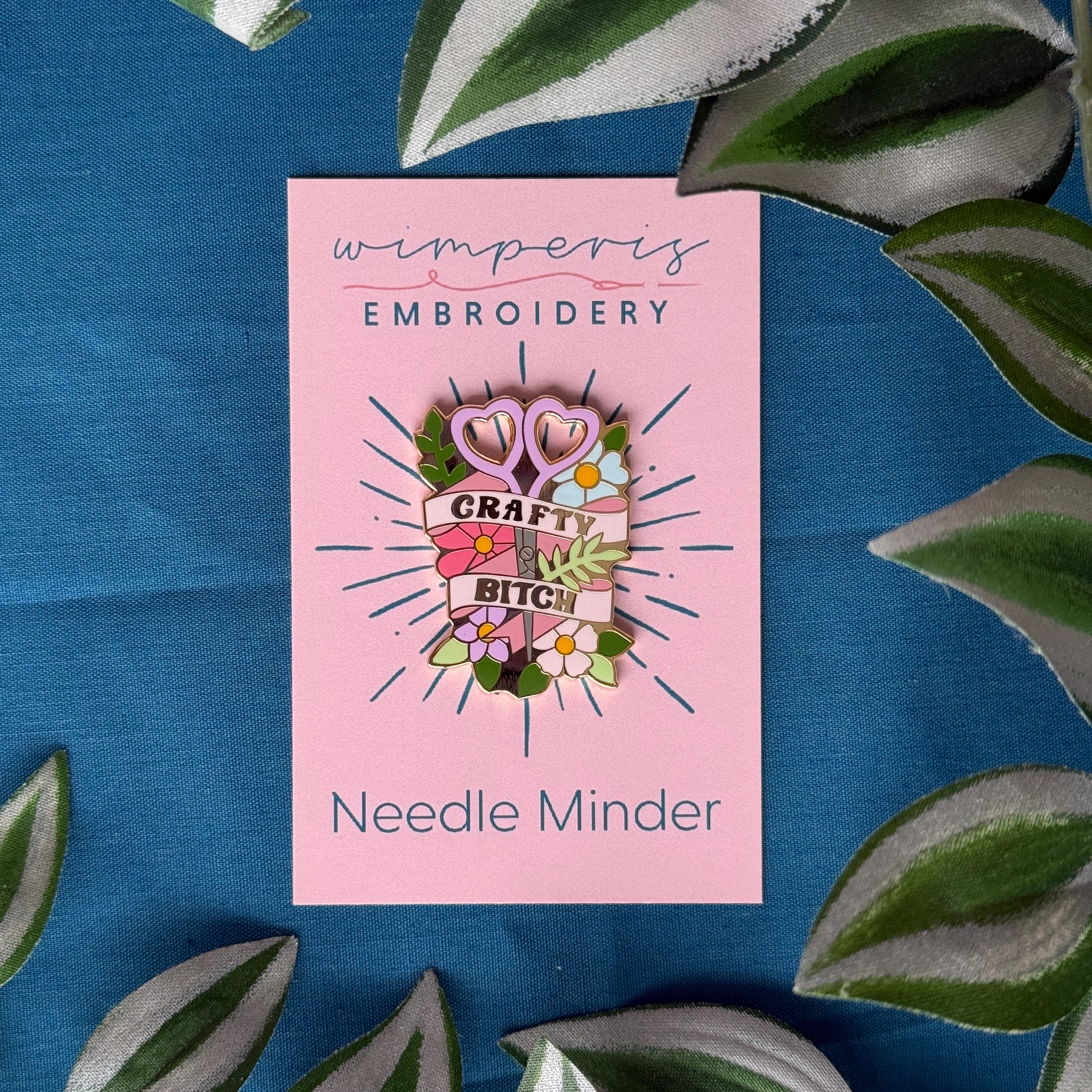 Pink needle minder with decorative design on a blue background with leaves