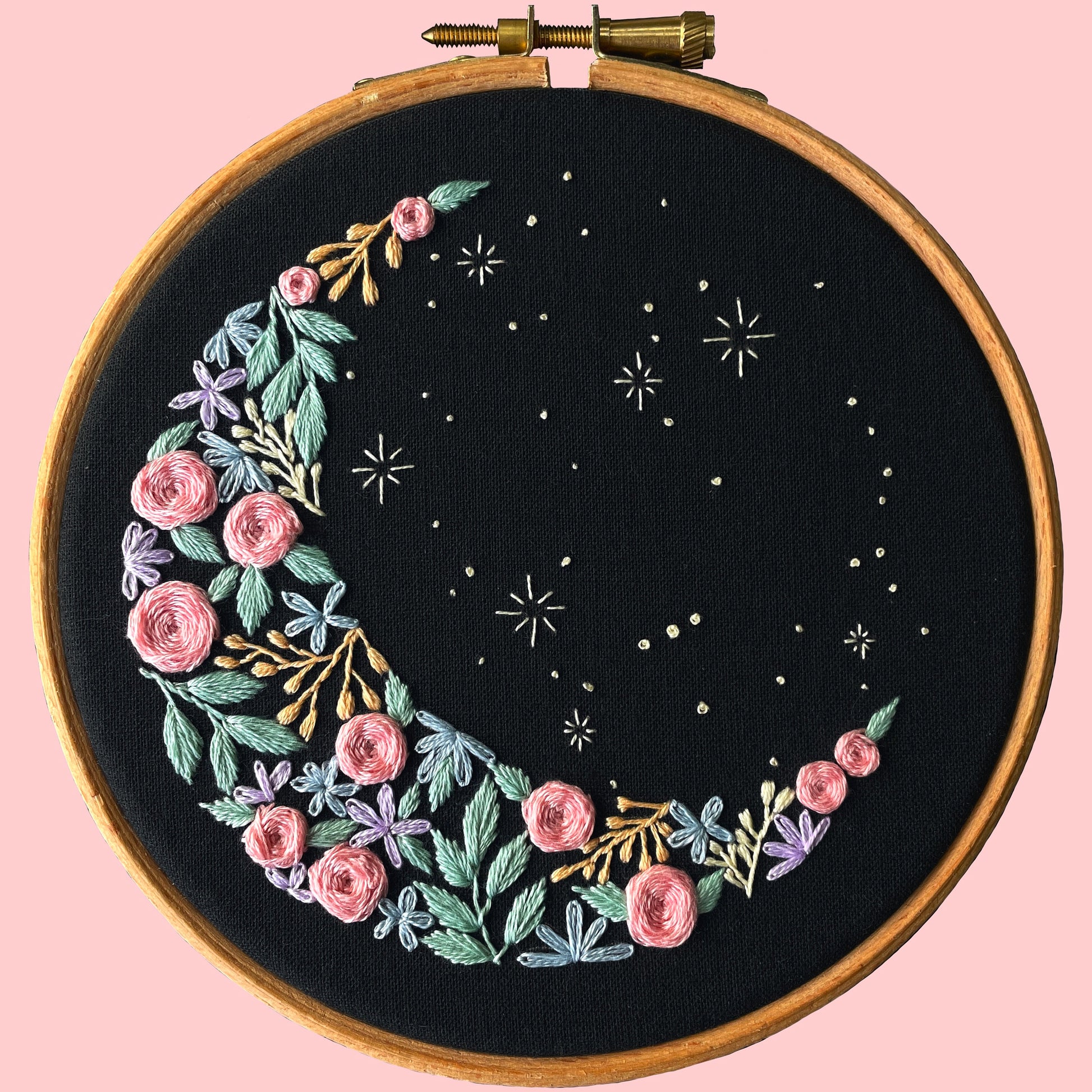 Embroidery kit showcasing a crescent moon shape on black fabric with floral embroidery and stars.