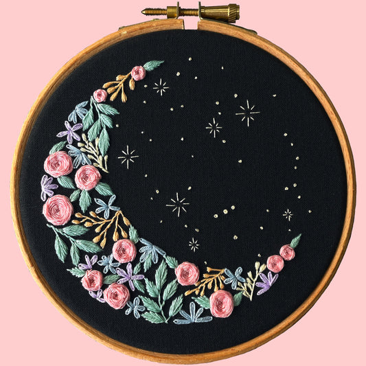 Embroidery kit showcasing a crescent moon shape on black fabric with floral embroidery and stars.